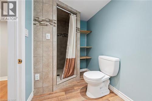 Three-piece bathroom featuring a tiled stand-up shower with mosaic accent, wood-finish flooring, built-in shelving, and light blue wall color - 838 Moore Street, Cambridge, ON - Indoor Photo Showing Bathroom