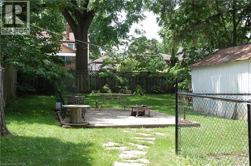 Expansive backyard featuring a concrete patio, a detached storage shed with a metal roof, mature trees, and a wooden privacy fence - 838 Moore Street, Cambridge, ON - Outdoor With Backyard