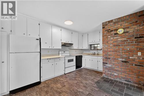 Kitchen featuring white cabinetry, light countertops, vinyl flooring, a built-in oven, and a brick accent wall with slate-style flooring - 1629 Gregory Road, St. Catharines, ON 