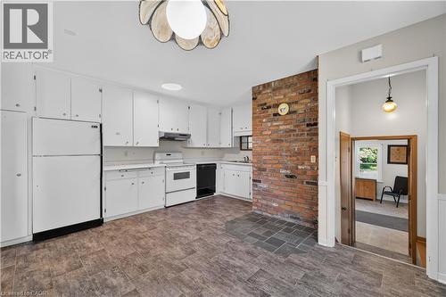 Kitchen featuring extensive white cabinetry, white appliances, a built-in dishwasher, and a brick accent wall - 1629 Gregory Road, St. Catharines, ON 