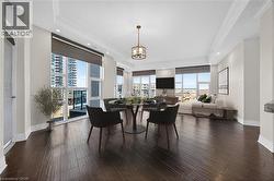 Expansive living area featuring rich wood-finish flooring, numerous large windows, a decorative chandelier, recessed lighting, and crown molding - 