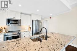 Spacious kitchen featuring white shaker cabinetry, stainless steel appliances, a light-toned tile backsplash, and a large island with an undermount double sink and dark bronze faucet - 