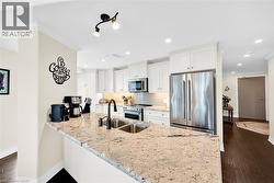 Modern kitchen featuring light-colored granite countertops, white cabinetry, stainless steel appliances, a tile backsplash, and dark wood-finish flooring - 