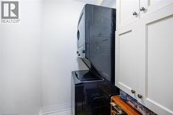 Laundry area with stacked black appliances, white shaker-style cabinetry, and light-toned flooring - 