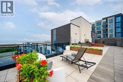 Expansive rooftop patio featuring a built-in outdoor kitchen, glass panel railings, and a mix of light-toned pavers and wood-finish flooring - 