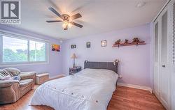 Bedroom featuring a large window, wood-finish flooring, a ceiling fan with integrated lighting, and louvered bi-fold closet doors - 