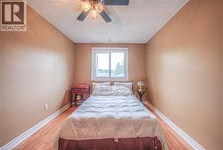 Room featuring a window, ceiling fan, and wood-finish flooring with white baseboards - 