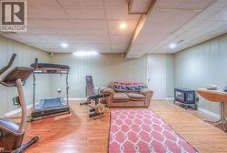 Finished lower level featuring wood-finish flooring, drop ceiling with recessed lighting, beadboard wall paneling, and a white interior door - 