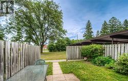 Private fenced patio area with a concrete walkway, bordered by lush green grass and mature trees - 