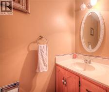 Bathroom vanity featuring wood-finish cabinetry, a white countertop with integrated sink, and an oval mirror with an ornate frame - 