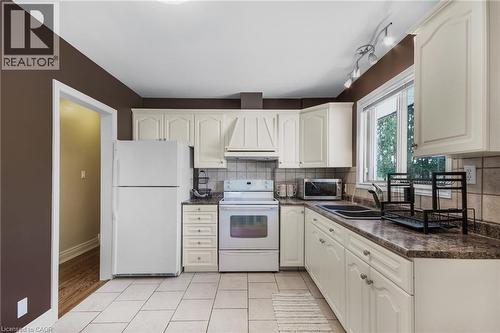 Bright kitchen featuring white cabinetry, a large window, tile flooring, track lighting, and white appliances - 185 Burlington Street, London, ON 