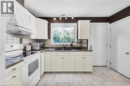 Kitchen featuring cream-colored cabinetry, tile flooring, granite-style countertops, a double basin sink, and a window with exterior visibility - 185 Burlington Street, London, ON 