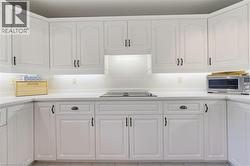 Kitchen featuring extensive white cabinetry, light countertops, an integrated cooktop, subway tile backsplash, and under-cabinet lighting - 