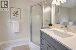 Bathroom featuring a frameless glass shower enclosure, a single vanity with a white countertop and integrated sink, a chrome faucet, and overhead vanity lighting - 