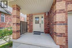 Inviting front porch featuring a multi-toned brick facade, covered entry, light-colored entry door with glass inserts, and a built-in wall sconce - 