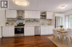 Modern kitchen featuring white cabinetry, stainless steel appliances, patterned tile backsplash, and wood-finish flooring - 