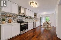 Open-concept kitchen with wood-finish flooring, white cabinetry, patterned tile backsplash, stainless steel appliances, and a dining area with patio door access - 
