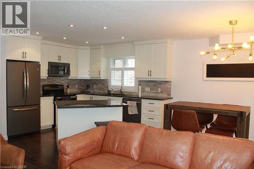 Open-concept kitchen featuring white cabinetry, dark stone countertops, a tile backsplash, and stainless steel appliances - 27 Stillwater Street, Kitchener, ON 