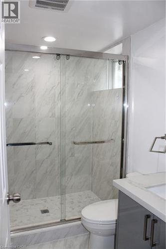 Shower enclosure with a clear glass sliding door, polished chrome hardware, and white marble-look tile - 27 Stillwater Street, Kitchener, ON 