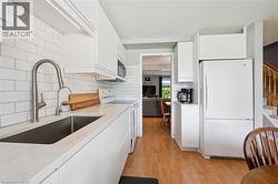 Kitchen featuring white flat-panel cabinetry, white subway tile backsplash, white countertops, and wood-finish flooring - 