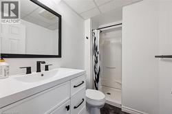 Bathroom featuring a white vanity with matte black hardware, a rectangular mirror, a white undermount sink with a matte black faucet, a white shower stall, and dark wood-finish flooring - 