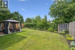 Expansive backyard featuring a lush lawn, a stone patio, and a gazebo with privacy curtains - 