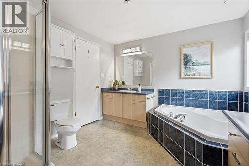 Spacious bathroom featuring a built-in corner bathtub with blue and black tile surround, a glass-enclosed shower, and a vanity with a dark countertop and light wood-finish cabinetry - 128 Houghton Street, Cambridge, ON 