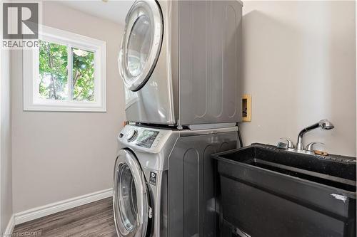 Dedicated laundry area featuring a stacked washer and dryer, a utility sink with a pull-out faucet, wood-finish flooring, and a window - 128 Houghton Street, Cambridge, ON 