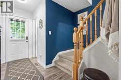 Entryway featuring a white door with an integrated window and horizontal blinds, wood-finish flooring, and a staircase with light wood banister and balusters - 
