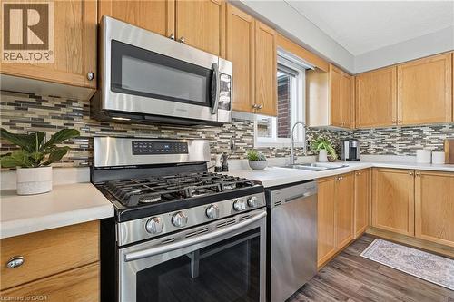 Kitchen featuring wood cabinetry, stainless steel appliances, a multi-tone tile backsplash, light-toned countertops, and wood-finish flooring - 128 Houghton Street, Cambridge, ON - Indoor Photo Showing Kitchen With Stainless Steel Kitchen With Double Sink