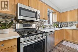 Kitchen featuring wood cabinetry, stainless steel appliances, a multi-tone tile backsplash, light-toned countertops, and wood-finish flooring - 