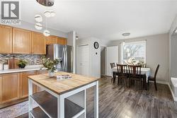 Open-concept kitchen and dining area featuring wood-finish flooring, light wood cabinetry, white countertops, a tiled backsplash, and stainless steel appliances - 