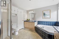 Spacious bathroom featuring a built-in corner bathtub with blue and black tile surround, a glass-enclosed shower, and a vanity with a dark countertop and light wood-finish cabinetry - 