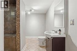 Bathroom featuring an enclosed shower with stone-look tile, mosaic tile accents, a track light fixture, a toilet, and a vanity with an integrated sink and mirror - 