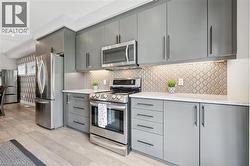 Contemporary kitchen featuring grey cabinetry, stainless steel appliances, patterned tile backsplash, white countertops, and wood-finish flooring - 