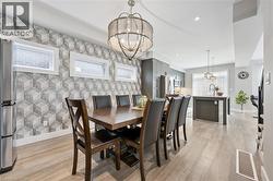 Open-concept dining area featuring wood-finish flooring, a contemporary chandelier, and geometric pattern wall covering - 