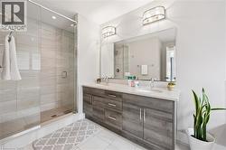Bathroom featuring a double vanity with wood-finish cabinetry, a large frameless mirror, and a glass-enclosed shower with tiled walls and a rain showerhead - 