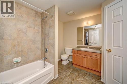 Bathroom featuring a bathtub with tiled surround, a wood-finish vanity with an integrated sink, a large wall-mounted mirror, and square floor tiling - 760 Paris Boulevard, Waterloo, ON 
