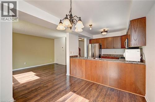 Open-concept living space featuring wood-finish flooring, a kitchen with wood cabinetry, stainless steel refrigerator, and stone countertops - 760 Paris Boulevard, Waterloo, ON 