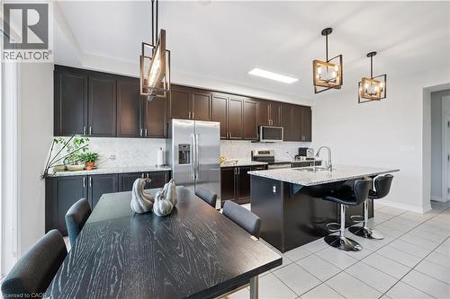 Kitchen featuring dark wood cabinetry, stainless steel appliances, a white tile backsplash, and a central island with bar seating - 87 Ridge Road, Cambridge, ON 