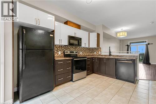 Kitchen featuring two-tone cabinetry with white upper and dark wood-finish lower units, a mosaic tile backsplash, and stone-finish countertops - 8 Hemlock Way Unit# 22, Grimsby, ON 