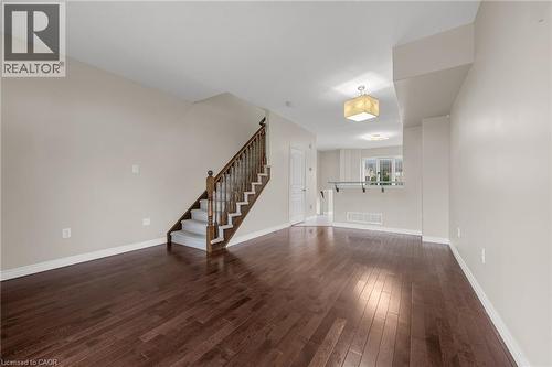 Expansive room featuring rich wood-finish flooring, a carpeted staircase with wood newel posts and balusters, light neutral wall paint, and a decorative ceiling light fixture - 8 Hemlock Way Unit# 22, Grimsby, ON 