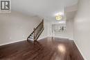 Expansive room featuring rich wood-finish flooring, a carpeted staircase with wood newel posts and balusters, light neutral wall paint, and a decorative ceiling light fixture - 8 Hemlock Way Unit# 22, Grimsby, ON 
