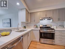 Modern kitchen featuring stainless steel appliances, light gray cabinetry, crisp white countertops, and a white marble-patterned backsplash - 