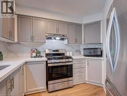 Contemporary kitchen featuring light gray cabinetry, stainless steel appliances, and wood-finish flooring - 