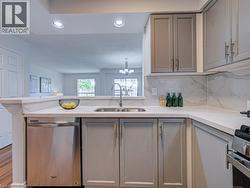 Modern kitchen featuring recessed lighting, light gray cabinetry, stainless steel sink, stainless steel dishwasher, and a light-colored countertop with a matching backsplash - 