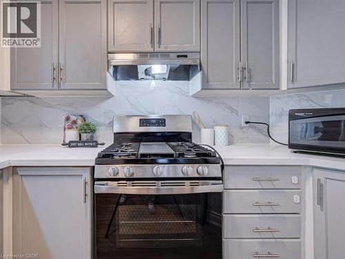 Stainless steel gas range with a matching range hood, surrounded by light gray cabinetry with brushed nickel hardware - 139 Werstine Terrace, Cambridge, ON 