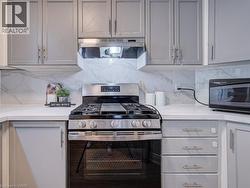 Stainless steel gas range with a matching range hood, surrounded by light gray cabinetry with brushed nickel hardware - 
