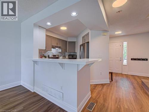 Kitchen pass-through with a breakfast bar, recessed lighting, wood-finish flooring, a stainless steel refrigerator, and a front entry door with sidelight - 139 Werstine Terrace, Cambridge, ON 