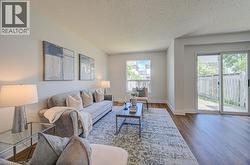 Open-concept living area featuring wood-finish flooring, a white trim baseboard, and a sliding glass door providing outdoor access - 